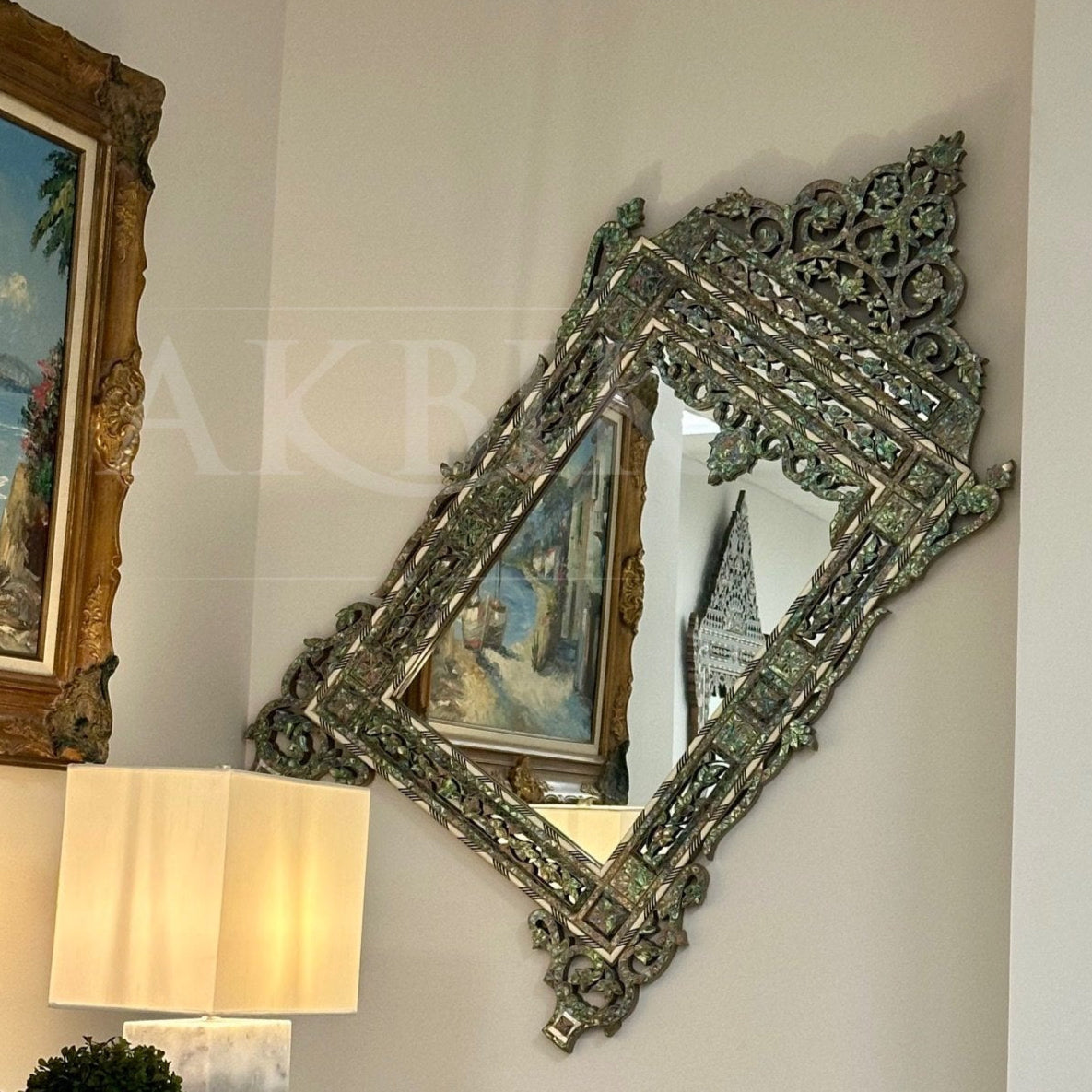 Decorative mirror with intricate design on a wall next to a lamp and framed picture.