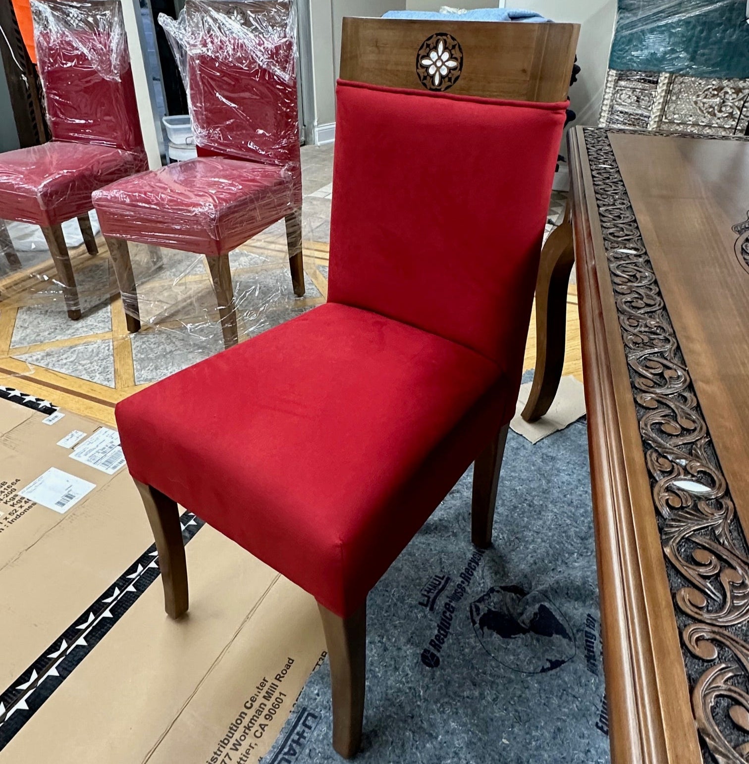 Red chair with wooden frame on a carpeted floor next to a cardboard box.