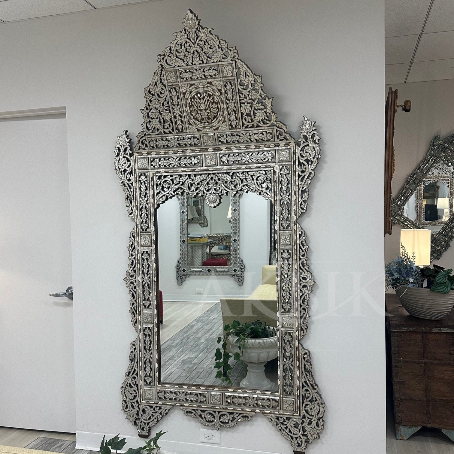 Decorative wall mirror with intricate patterns on a white wall.