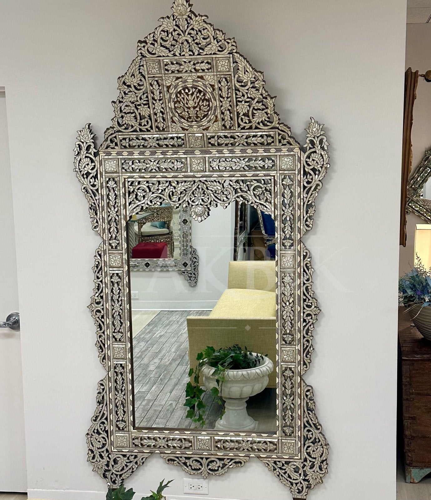 Decorative silver mirror with intricate patterns on a white wall.