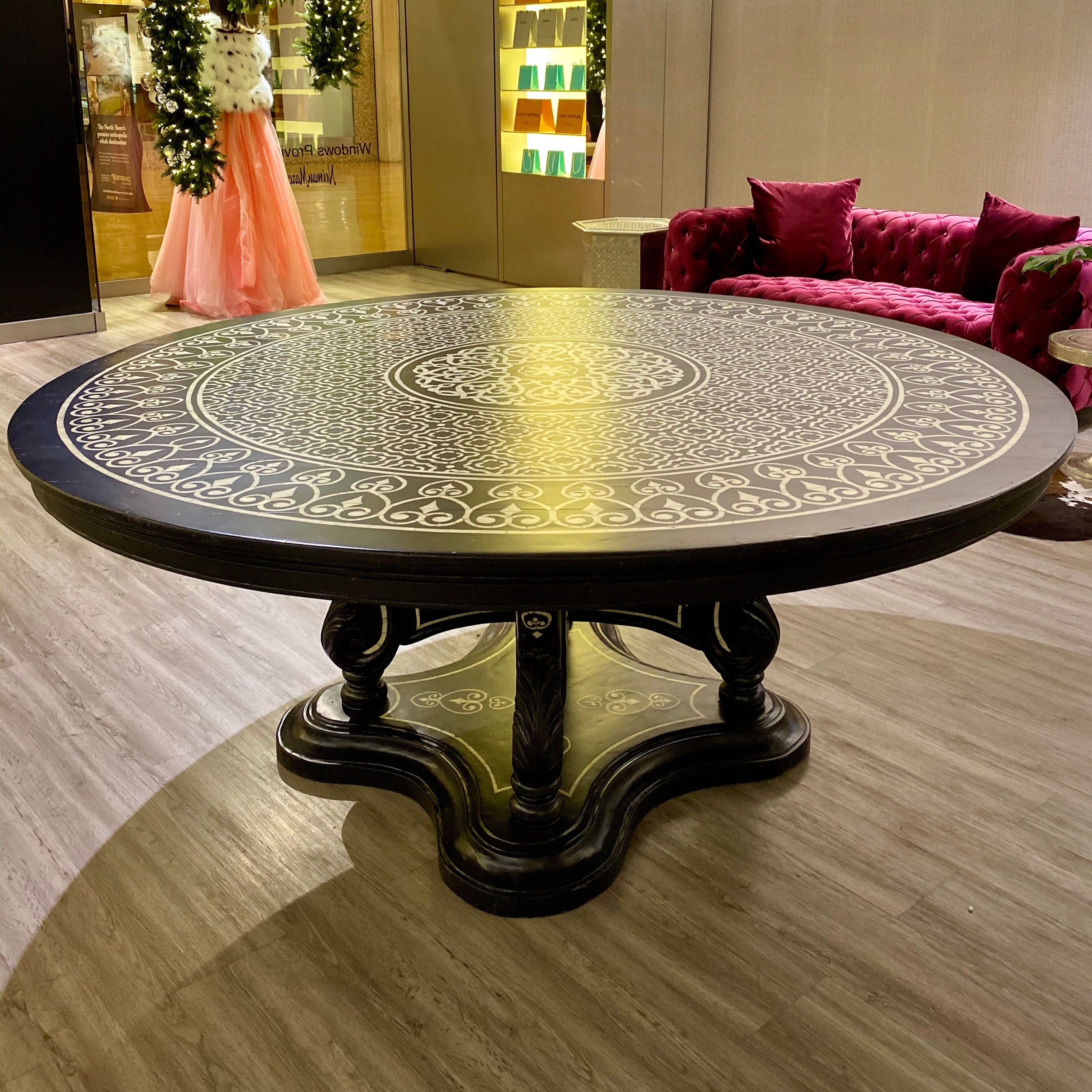 Round decorative table inlaid with mother of pearl in a stylish room with a pink sofa and floral decorations.