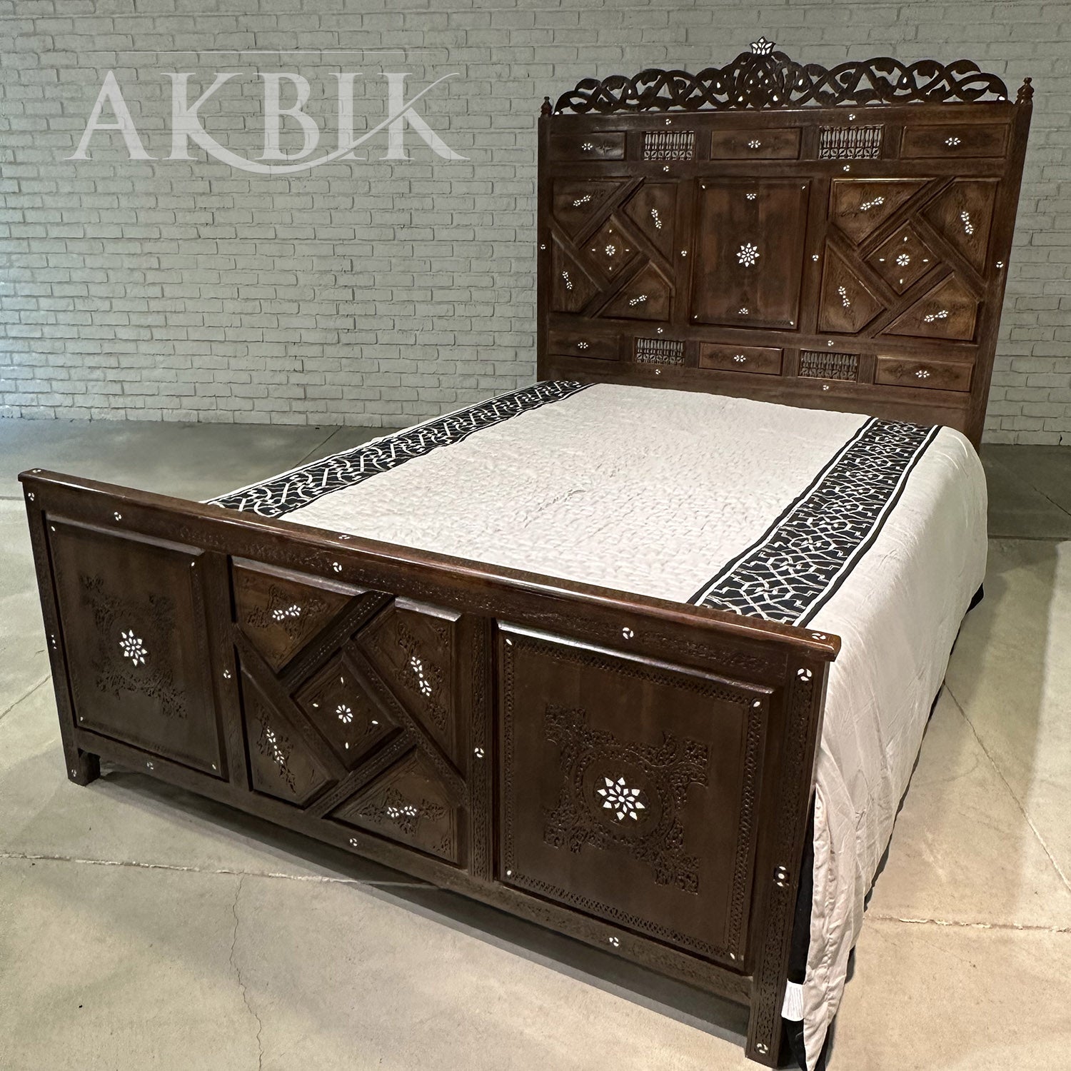 A hand-carved Syrian walnut bed with a detailed headboard and footboard, inlaid with mother of pearl, placed against a white background.