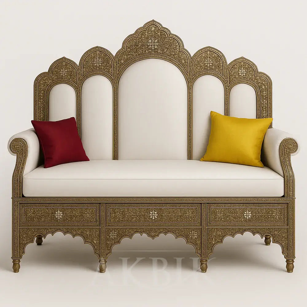 An ornately hand-carved Sultan-style sofa with a white upholstered backrest and seat, accented with a red and a yellow throw pillow, featuring intricate floral and arabesque carvings with a gold wax polish finish.